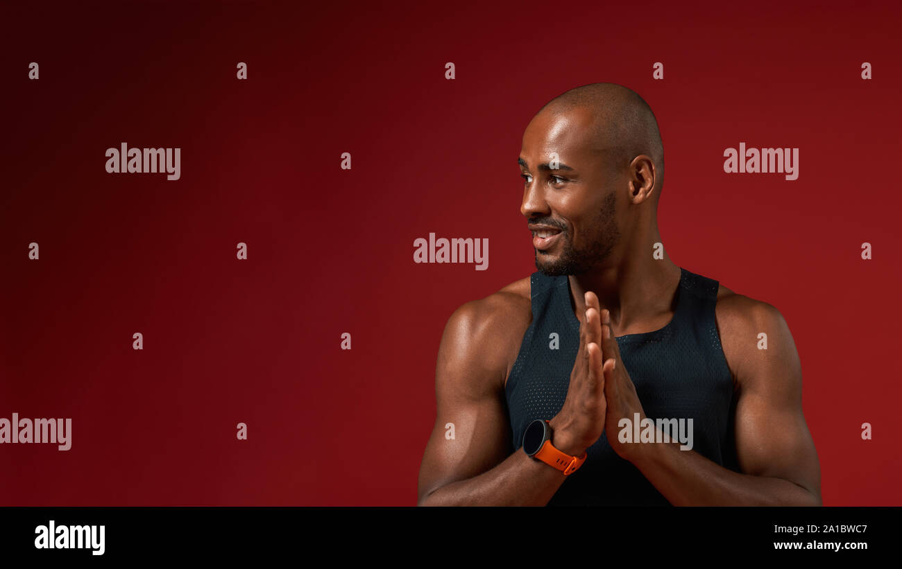 Io amo lo yoga. Giovani afro-americano mantenendo le palme insieme e guardando a parte con sorriso mentre in piedi contro lo sfondo di colore rosso. Concetto di Yoga Foto Stock