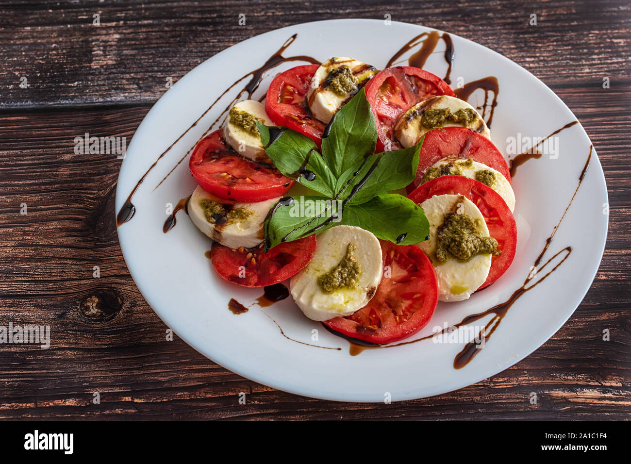 Piastra bianca di sana classic deliziosa insalata caprese con pomodoro e mozzarella con foglie di basilico e strisce di salsa di soia sul legno Foto Stock