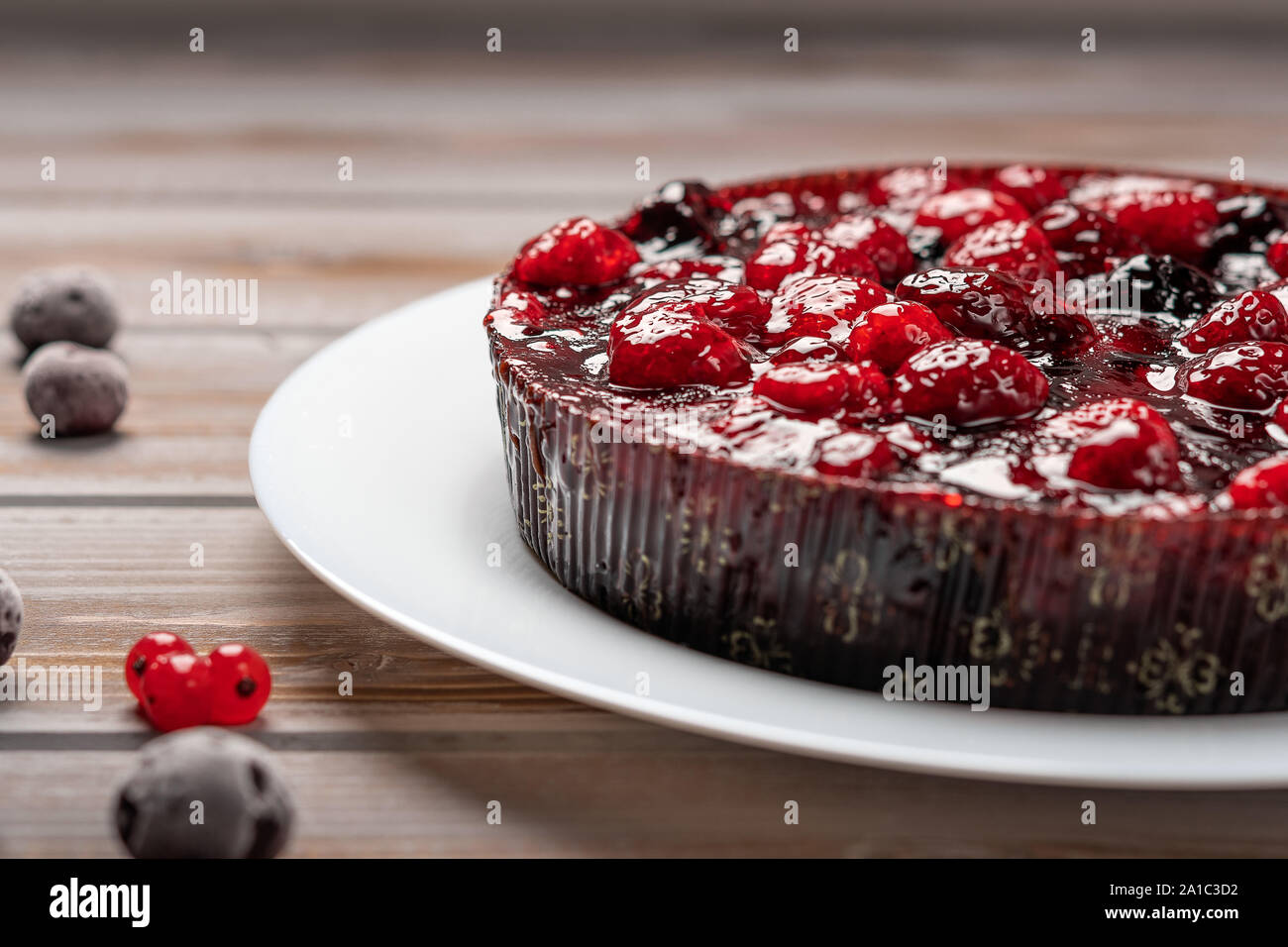 Torta con bacche di close-up: lampone, ribes, fragole su una piastra bianca su uno sfondo di legno, nei pressi di ribes rosso e ciliegia Foto Stock