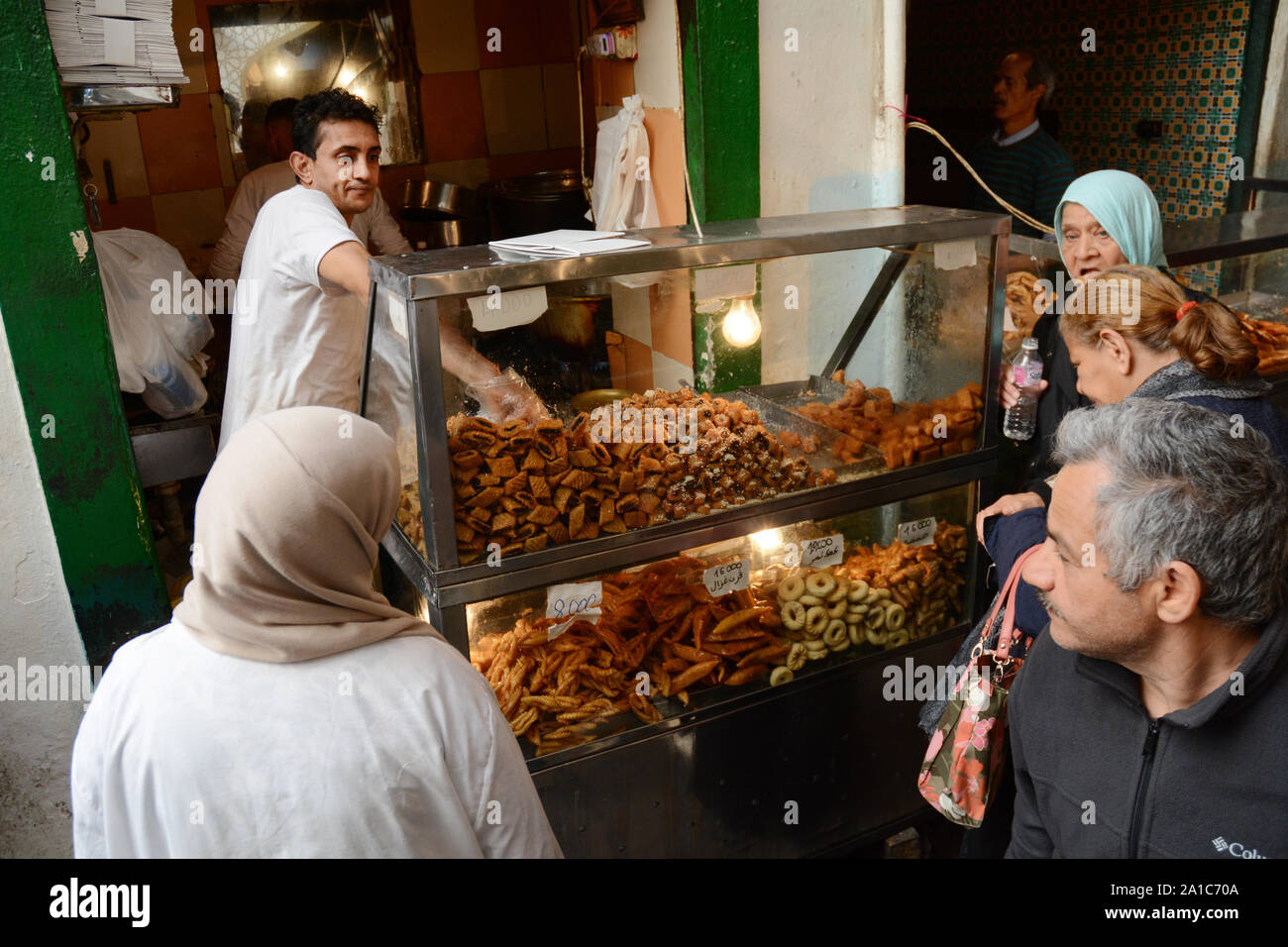 Un commerciante di alimentare la vendita di caramelle, biscotti e pasticcini serve i clienti in attesa nel mercato della Kasbah, nella medina di Tunisi, Tunisia. Foto Stock