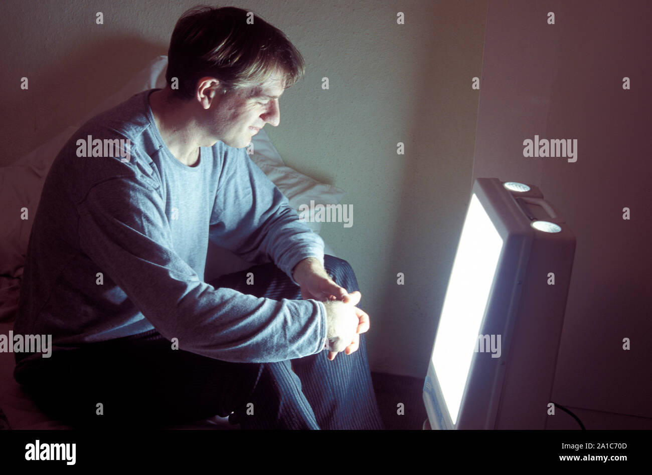 Giovane uomo nella parte anteriore della lampada triste in una stanza buia Foto Stock