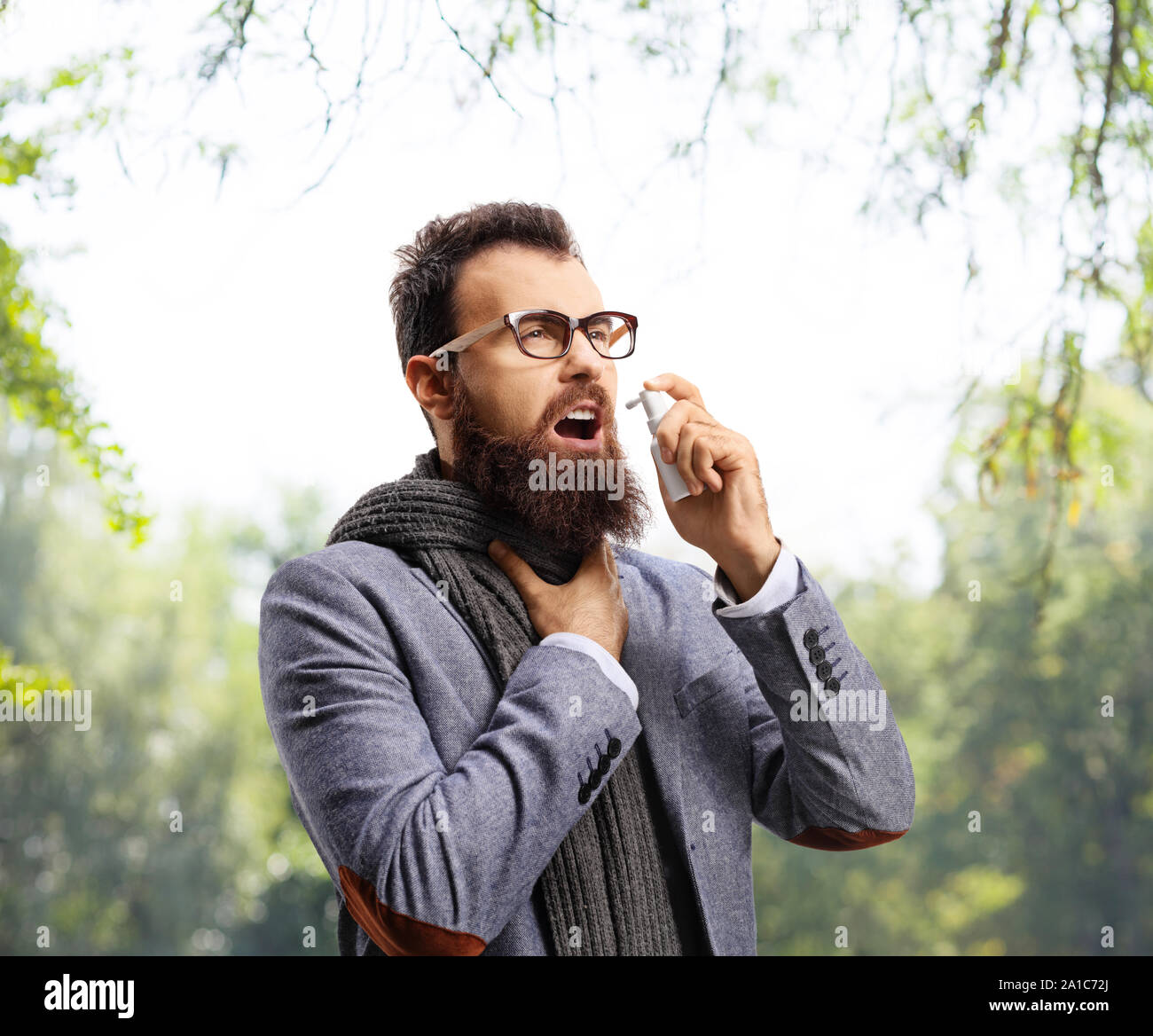 Uomo con una allergia la spruzzatura di un farmaco nella sua gola all'aperto Foto Stock