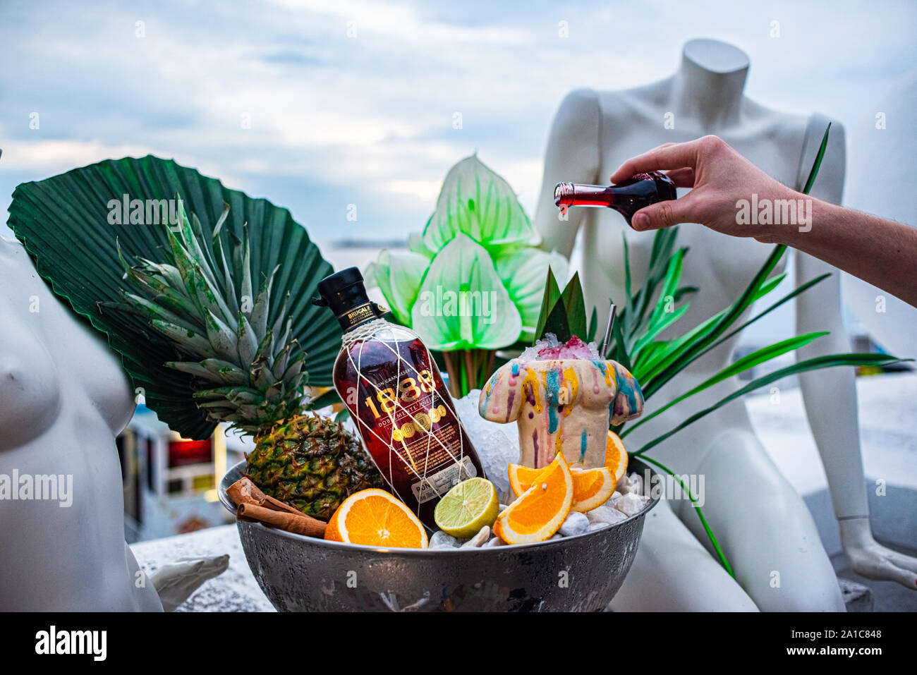 Shot promozionale di rum di ciotola con ghiaccio foglie di palmo ananas orange mano del barista. Foto Stock