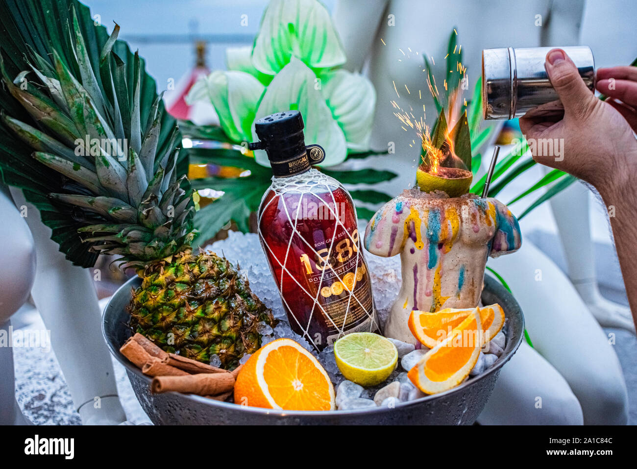Shot promozionale di rum di ciotola con ghiaccio foglie di palmo ananas orange mano del barista. Foto Stock
