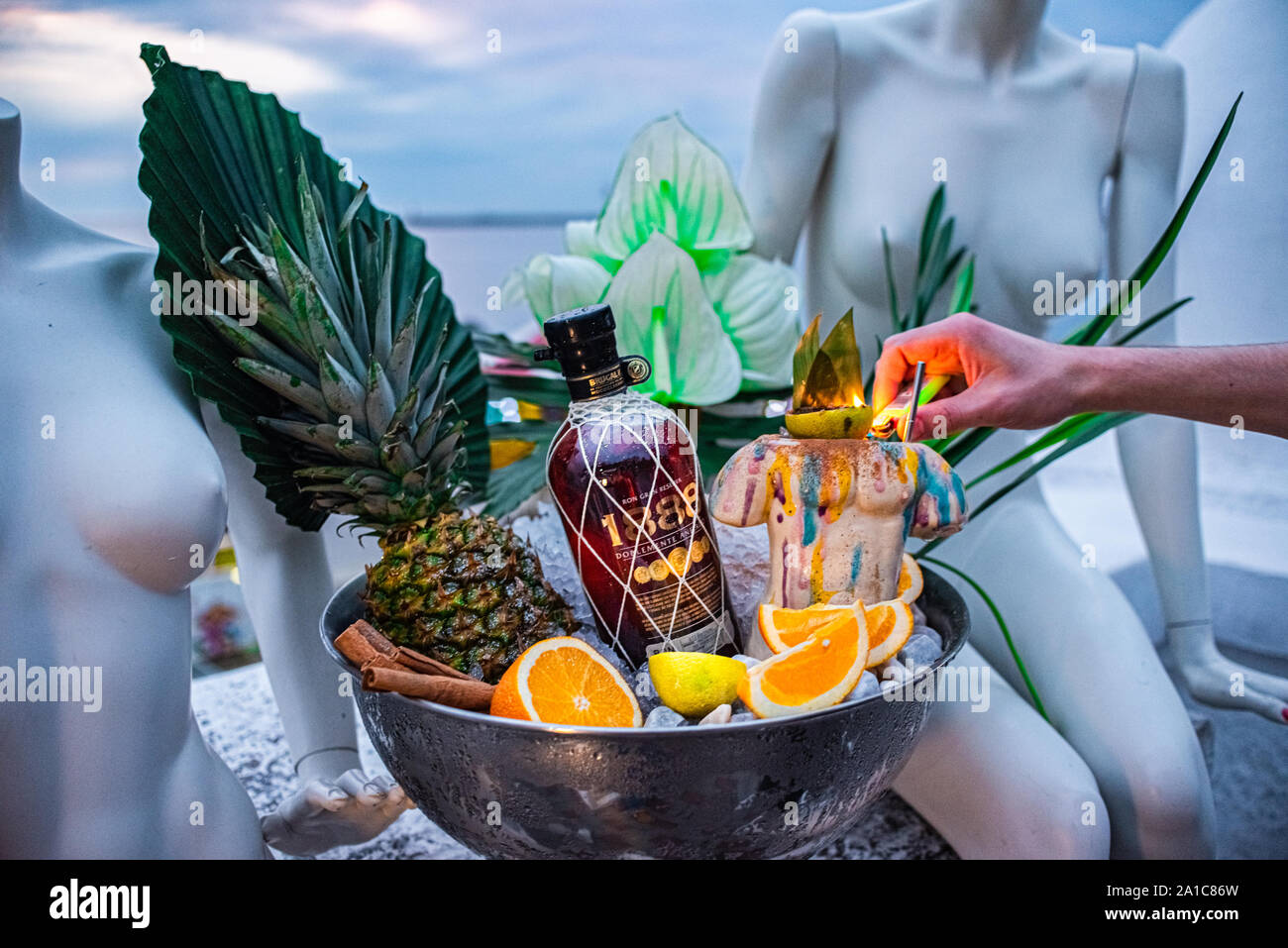 Shot promozionale di rum di ciotola con ghiaccio foglie di palmo ananas orange mano del barista. Foto Stock