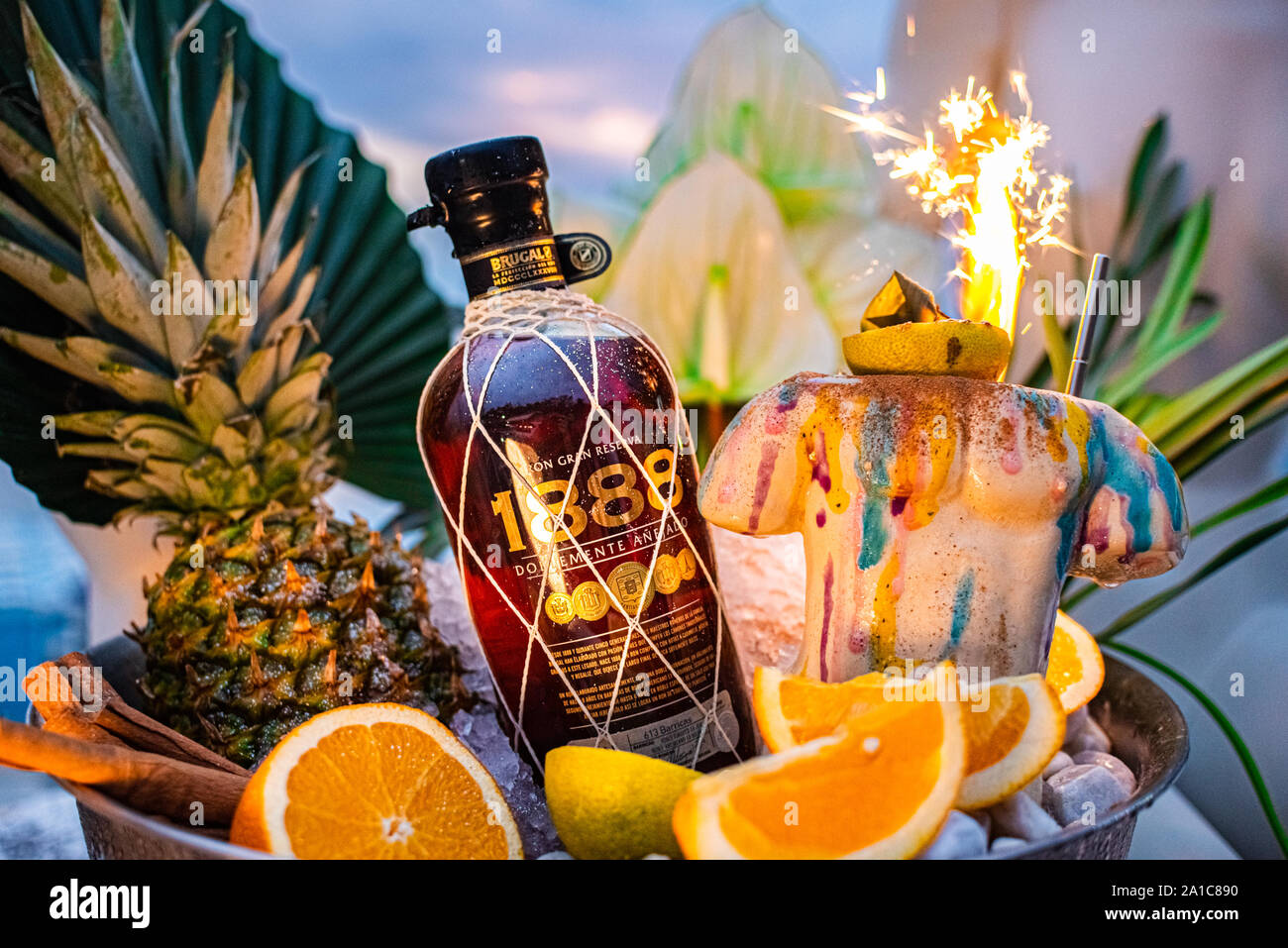 Shot promozionale di rum di ciotola con ghiaccio foglie di palmo ananas orange fuochi d'artificio. Foto Stock