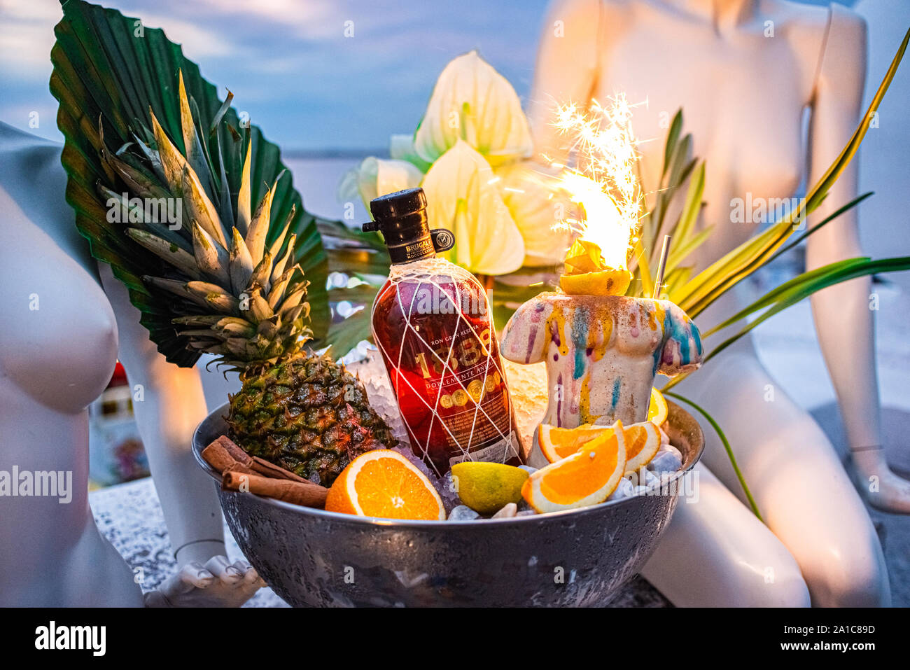Shot promozionale di rum di ciotola con ghiaccio foglie di palmo ananas orange fuochi d'artificio. Foto Stock