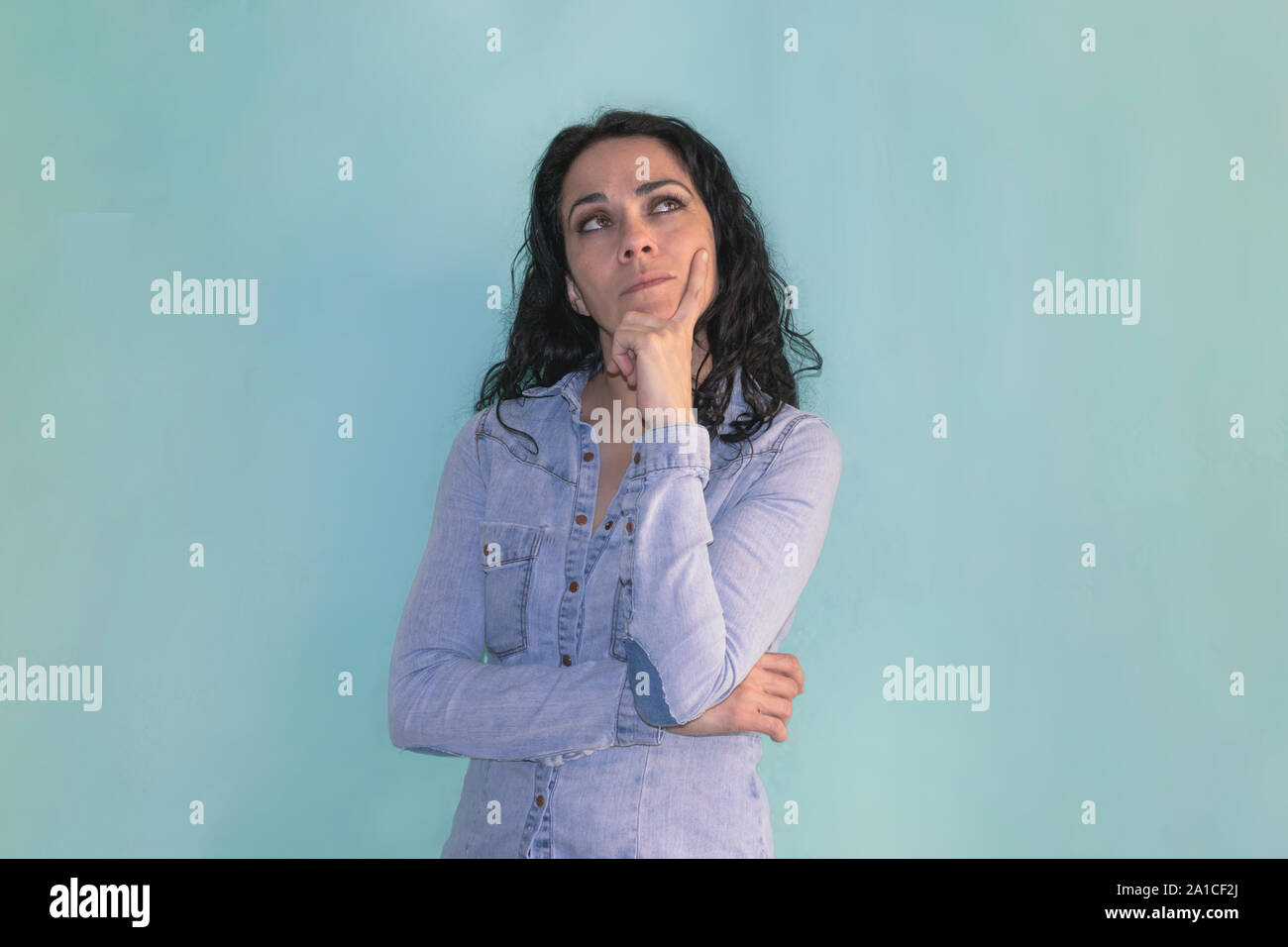 Brunette donna con la sua mano sulla mento, pensando a qualche questione, isolata su uno sfondo blu Foto Stock