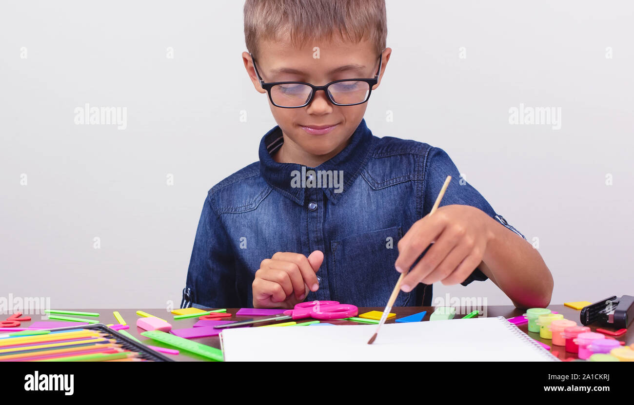 Banner ragazzo in una camicia blu e i bicchieri si siede a un tavolo su uno sfondo bianco. Attività Creative hobby disegno Foto Stock