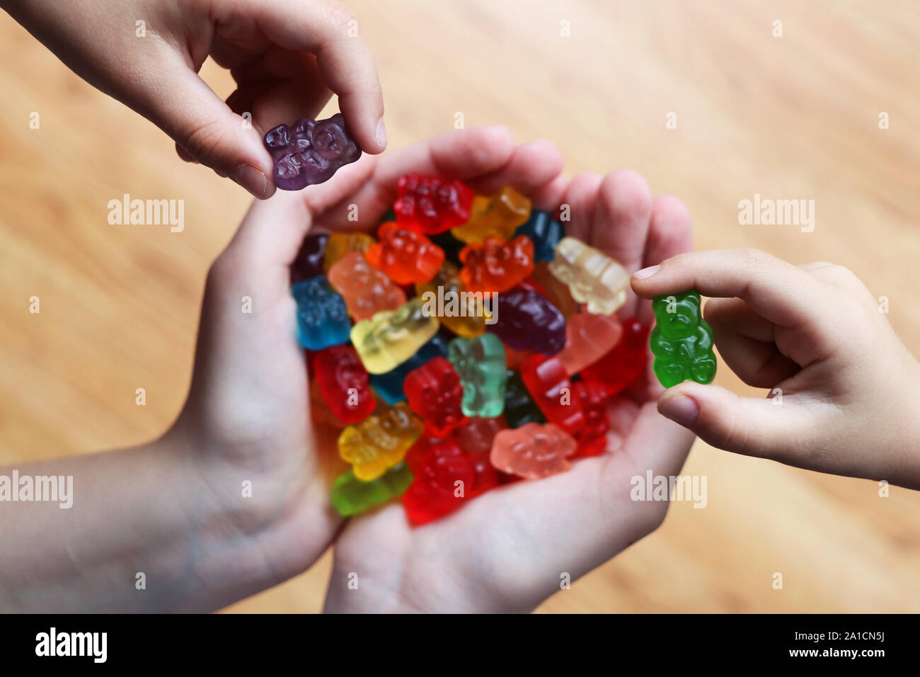 Una manciata di colorato e dolce orsi gommoso e due bambini mani raccogliendo i loro sapore preferito fuori Foto Stock