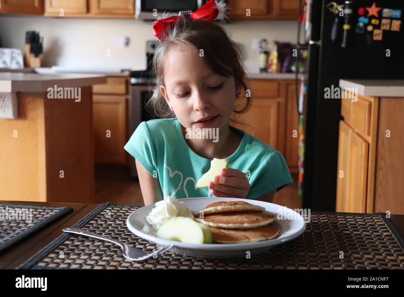 Bambino seduto al tavolo per mangiare frittelle e mele Foto Stock