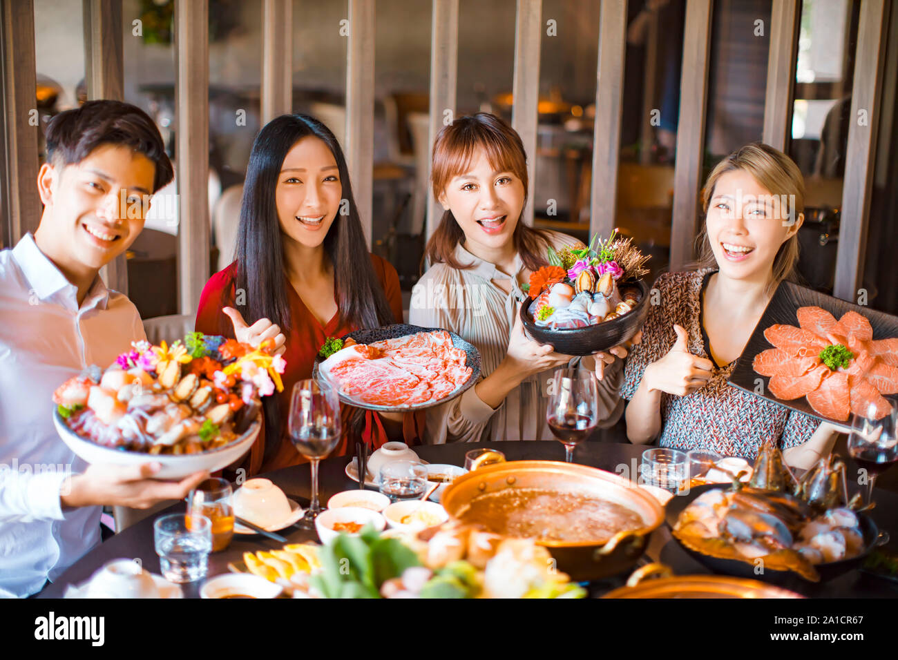 Giovani amici che mostra di frutti di mare e carne di maiale in fette hot pot restaurant Foto Stock