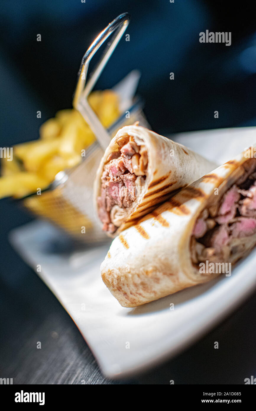 Un'immagine ravvicinata di un filetto alla griglia steak Tortilla avvolgere cucinato alla perfezione e serviti con una porzione di patate fritte Foto Stock