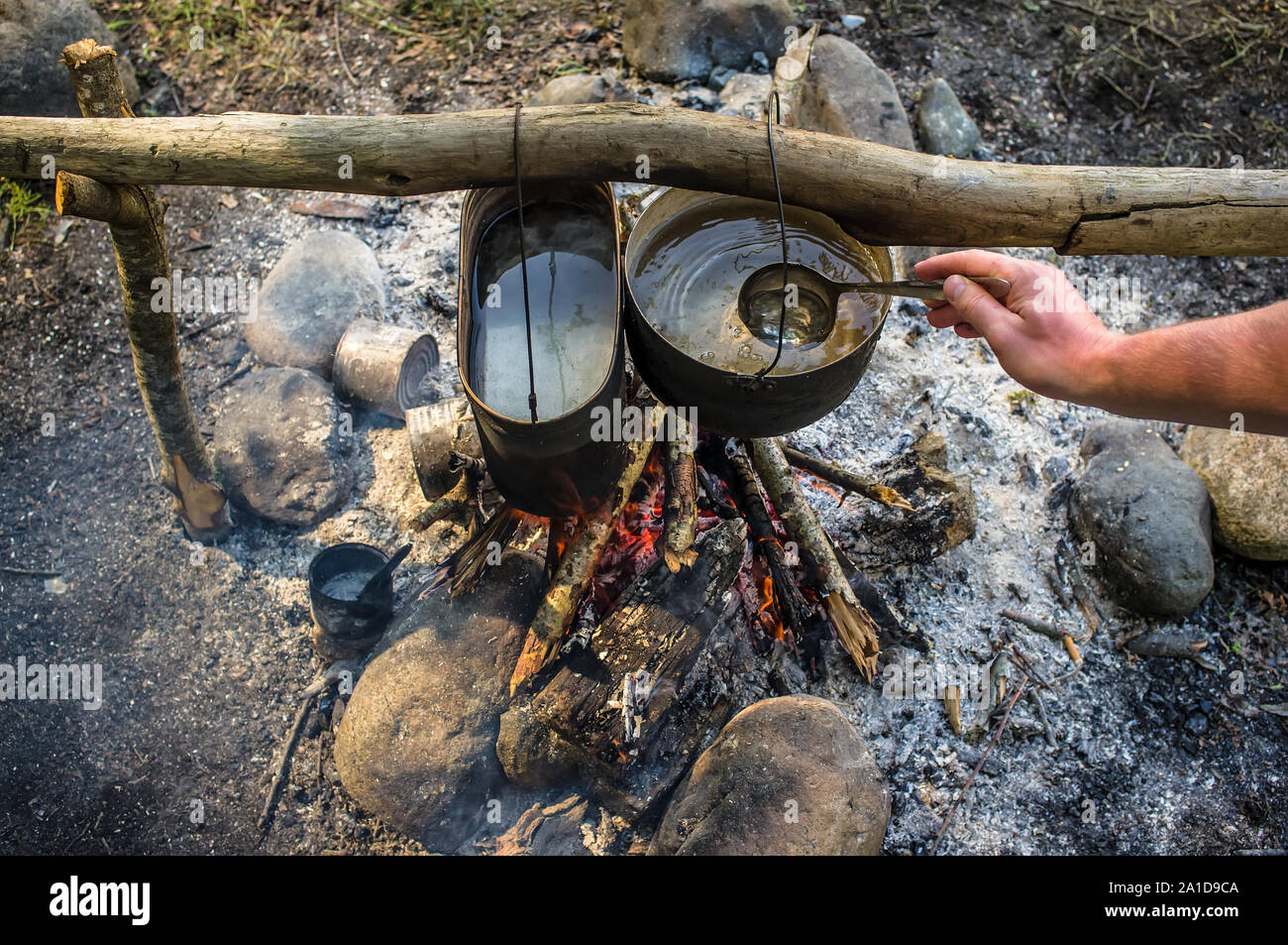 Vista superiore dell'uomo suscita mestolo di acqua che viene preparato in una escursione nella cauldrons, appeso sopra il fuoco Foto Stock