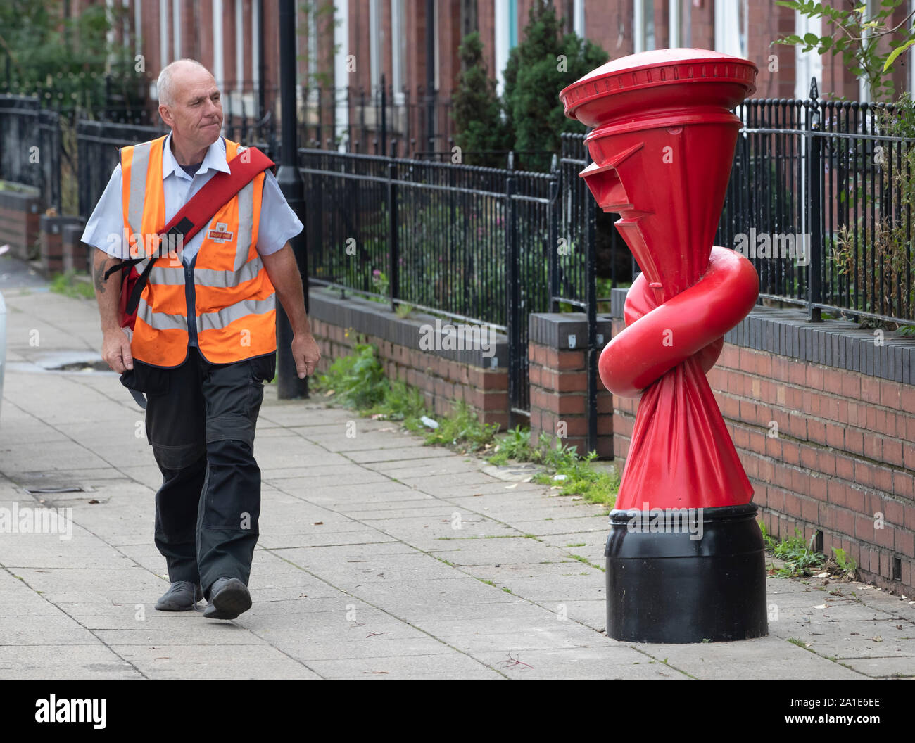 Un postino passeggiate passato un'arte lavoro intitolato Alphabetti Spaghett dall artista Alex Chinneck sulla strada Norborough in Sheffield, Yorkshire. Foto Stock