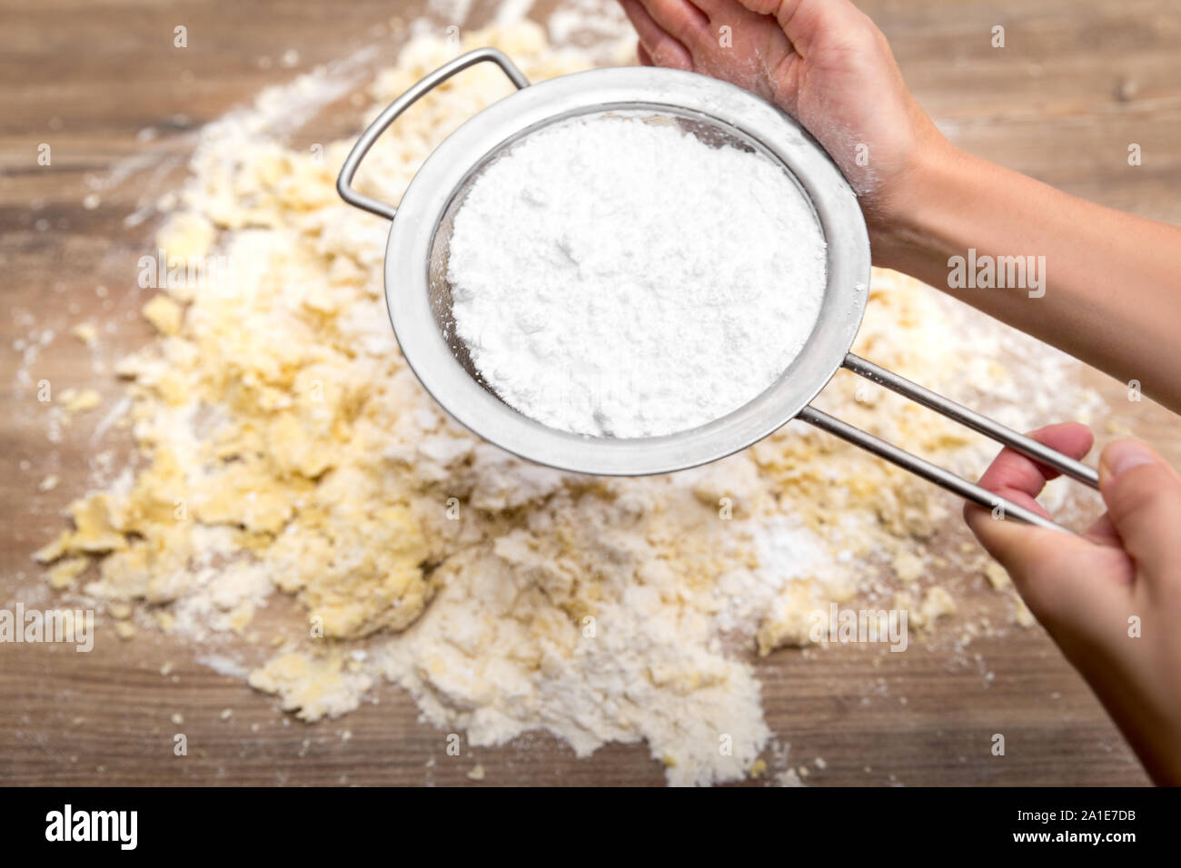 Donna setacciatura di zucchero a velo su una torta di greggio o pasta biscotto, passo da forno Foto Stock