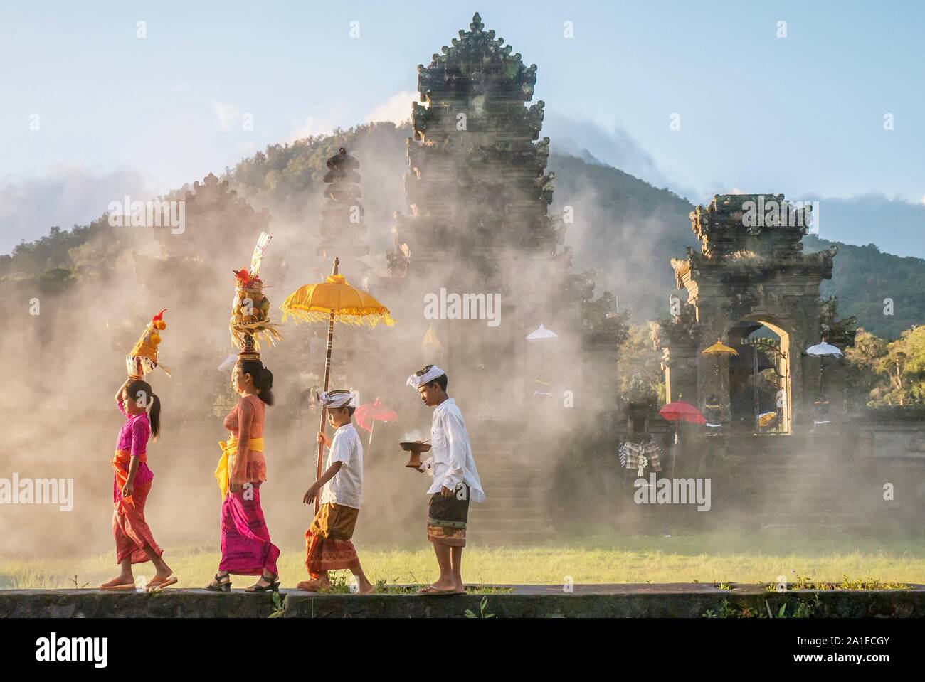 Mostra stile Balinese tradizionale maschio e femmina abiti cerimoniali e offerte di religiosi, come una madre e bambini a piedi a un tempio indù (pura). Foto Stock