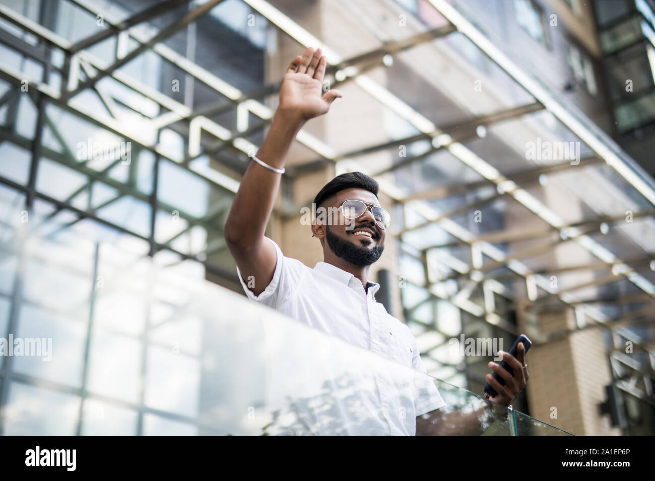 Grave imprenditore indiano in occhiali cercando su copia spazio mentre in piedi contro il grattacielo di vetro salutando a qualcuno. Foto Stock