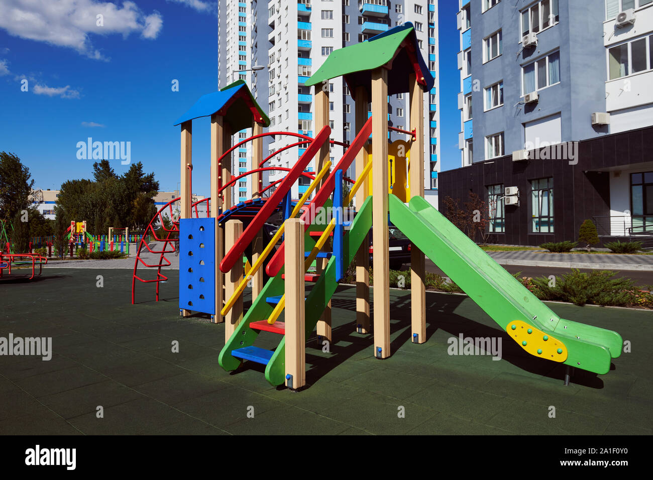 Vuoto in legno colorato per bambini con scorrimento scala sul parco giochi. Attrazioni situate nel cortile contro un alto edificio e cielo blu. Foto Stock