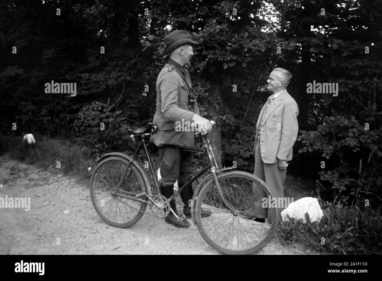 Ein Förster bei seinem Fahrrad unterhält sich mit einem älteren Herrn am Wegesrand, Deutschland 1939. Una foresta operaio con la sua bicicletta a parlare con un anziano uomo che ha incontrato sul suo cammino, Germania 1939. Foto Stock