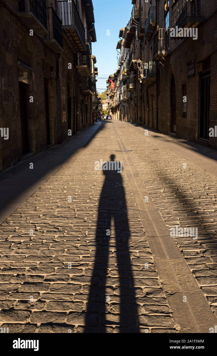 Fotografo scatta una foto della sua lunga ombra su una strada di ciottoli di Puente La Reina - Gares, Navarra, Spagna Foto Stock