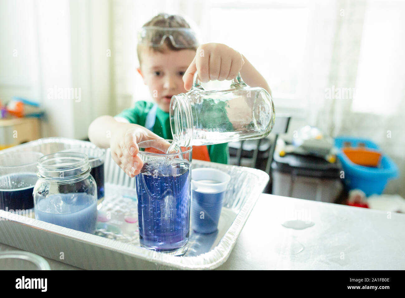 Elementare ragazzo di età versa acqua in un bicchiere mentre si fa un progetto di stelo Foto Stock