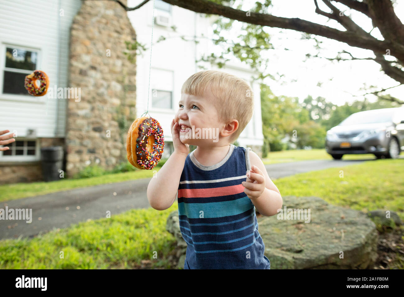 Felice toddler boy sorrisi mentre cercando di mangiare ciambella durante il party game Foto Stock