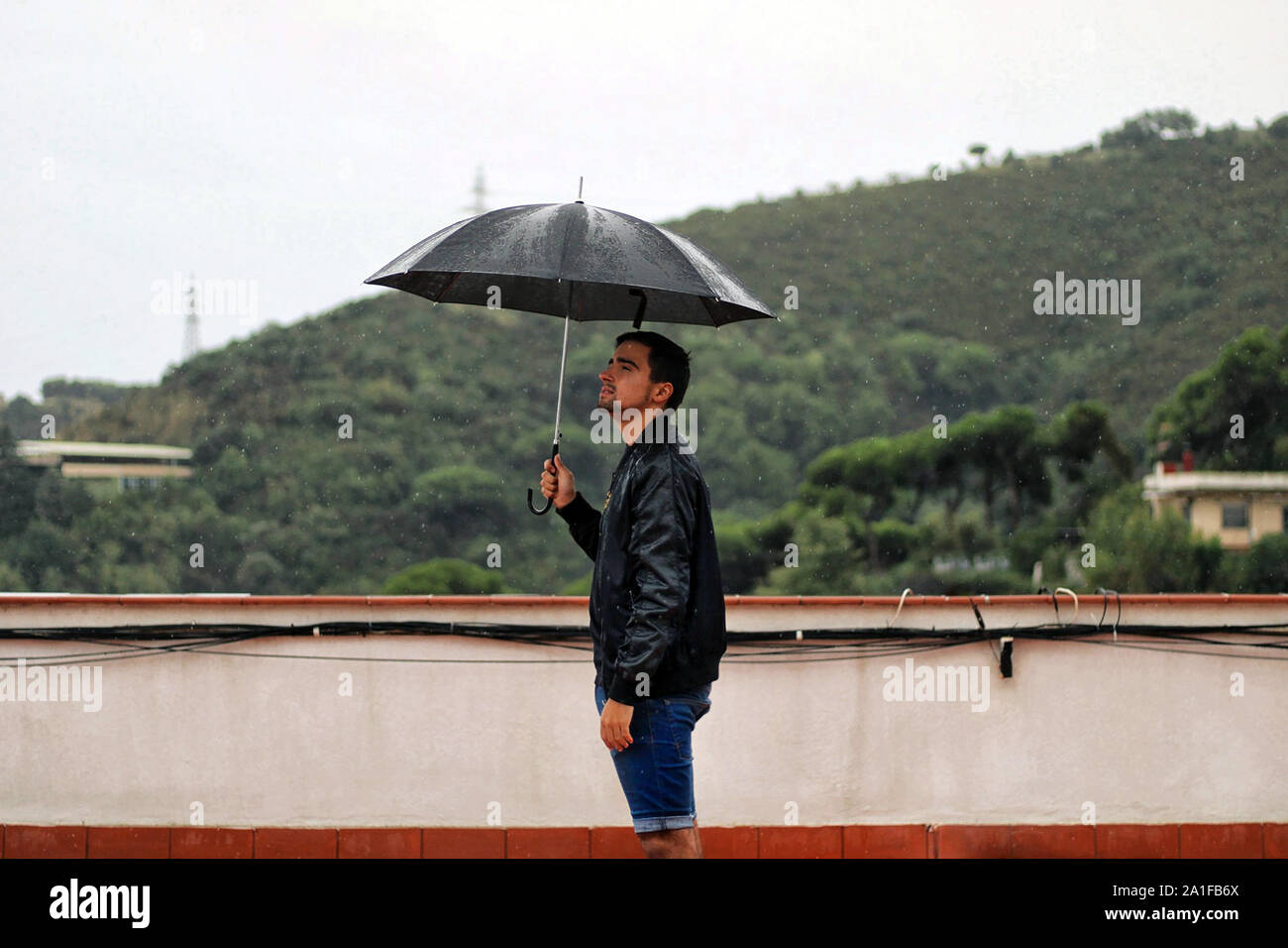Uomo con una giacca di pelle mantiene aperto il nero ombrello in mano sotto  la pioggia. Dietro il ragazzo si trova la montagna Foto stock - Alamy