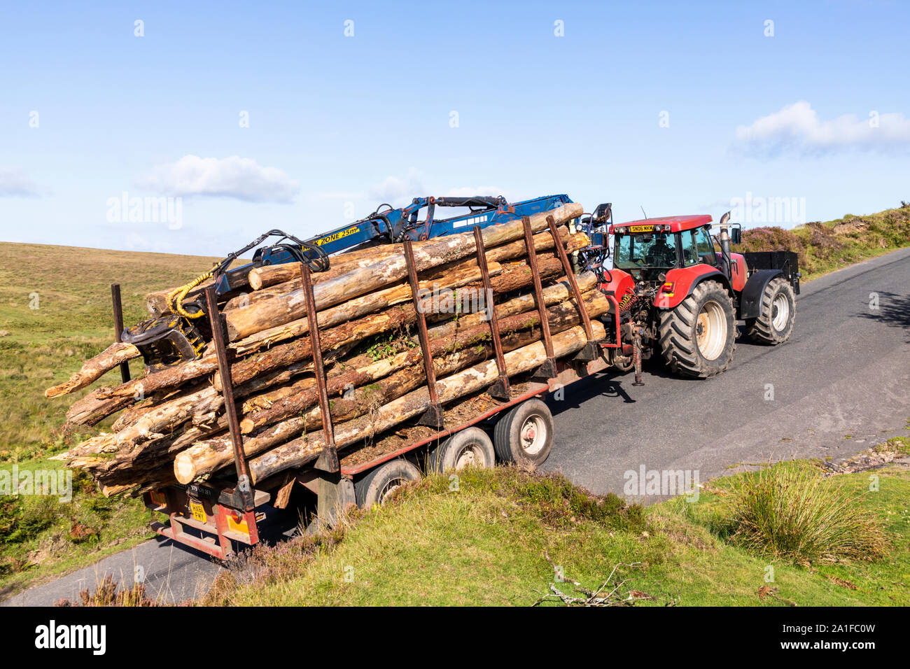 Un trattore che traina un rimorchio con un pesante carico di tronchi fino alla cima di una collina su Exmoor sopra la valle di acqua Chetsford a nord di Exford, Somerset REGNO UNITO Foto Stock