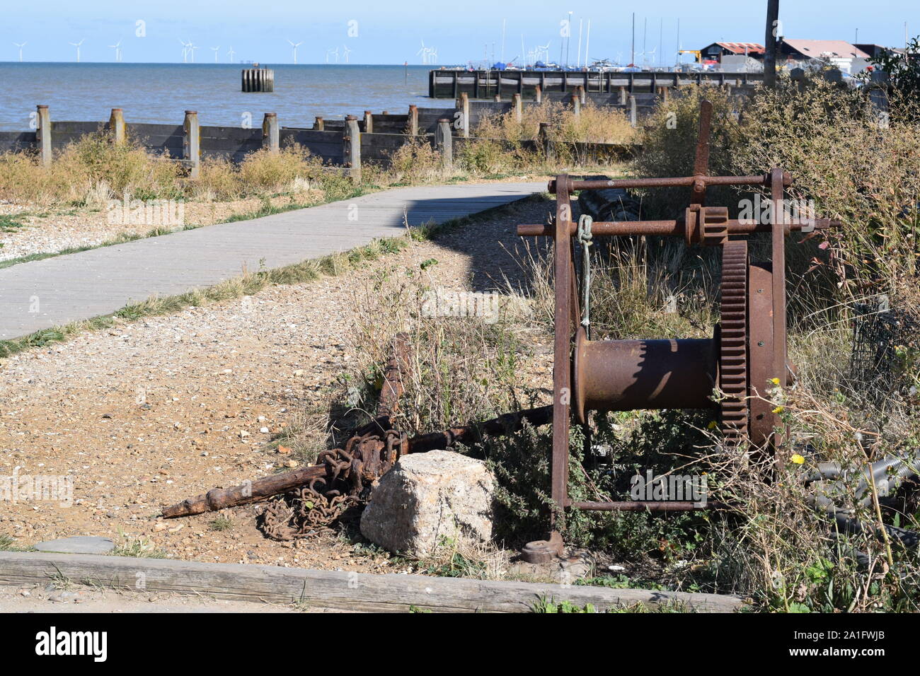 Il vecchio metallo arrugginito verricello in barca sulla spiaggia con il porto e il mare per centrali eoliche in distanza in estuario del Tamigi Foto Stock