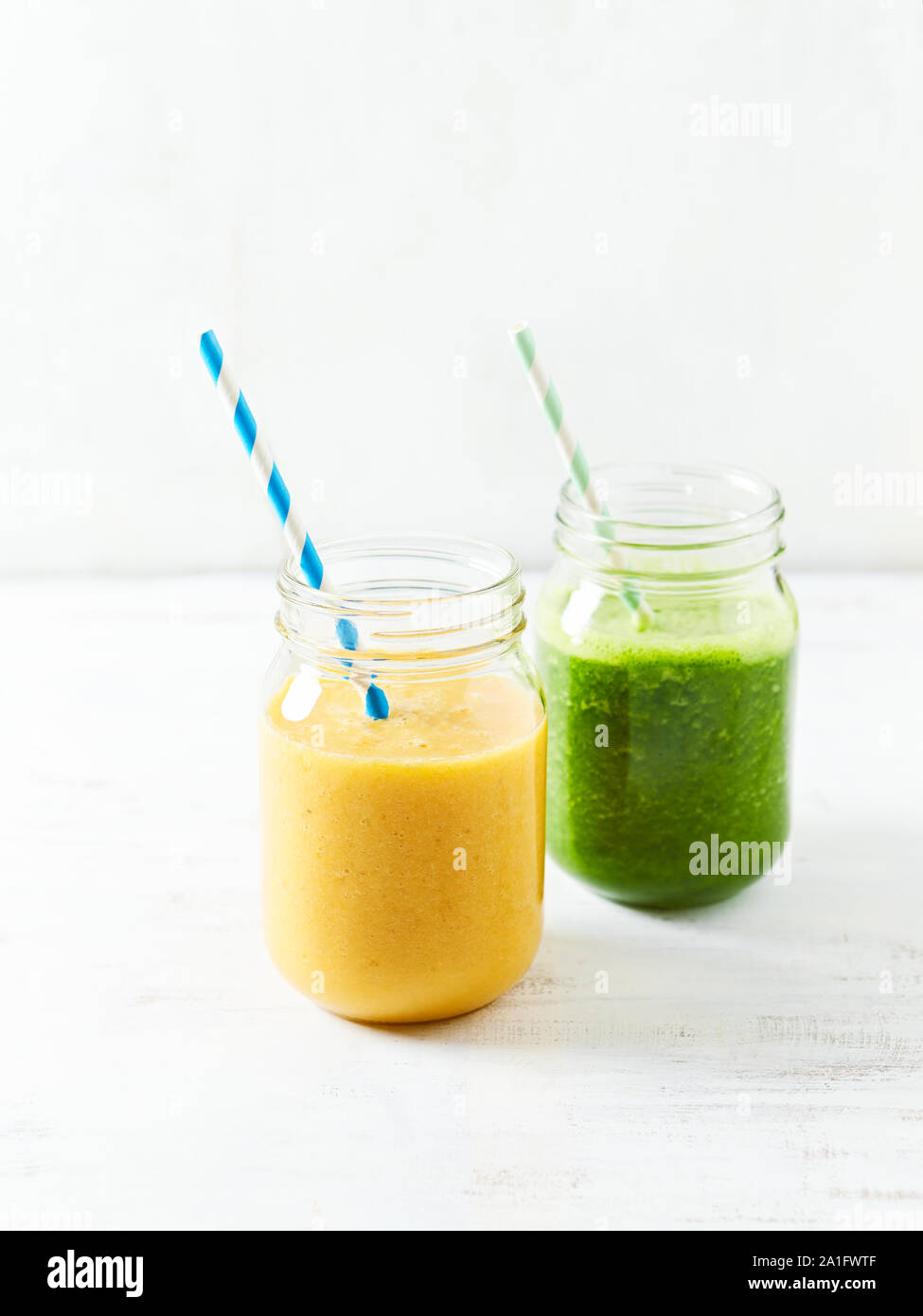 Banana-arancio e banana-kale smoothie in bicchieri. Immagine simbolica. Concetto di alimentazione sana. Sfondo bianco. Copia dello spazio. Foto Stock