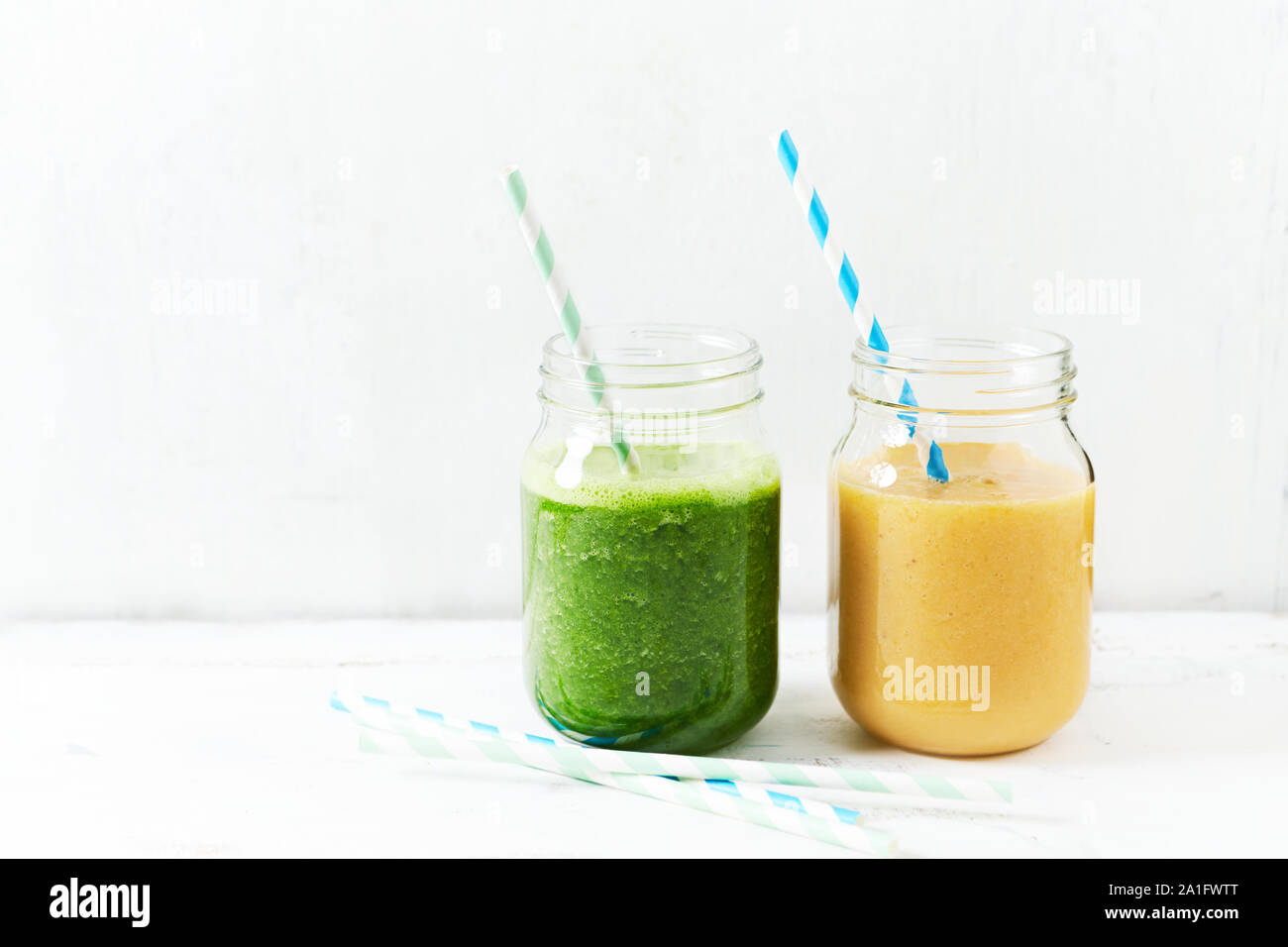 Banana-arancio e banana-kale smoothie in bicchieri. Immagine simbolica. Concetto di alimentazione sana. Sfondo bianco. Copia dello spazio. Foto Stock