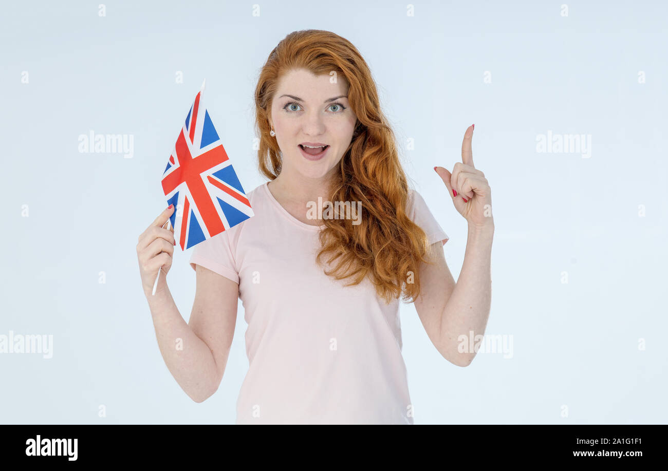 Dai capelli rossi giovane donna con la bandiera della Gran Bretagna punti il suo dito, in piedi su uno sfondo luminoso. Foto Stock