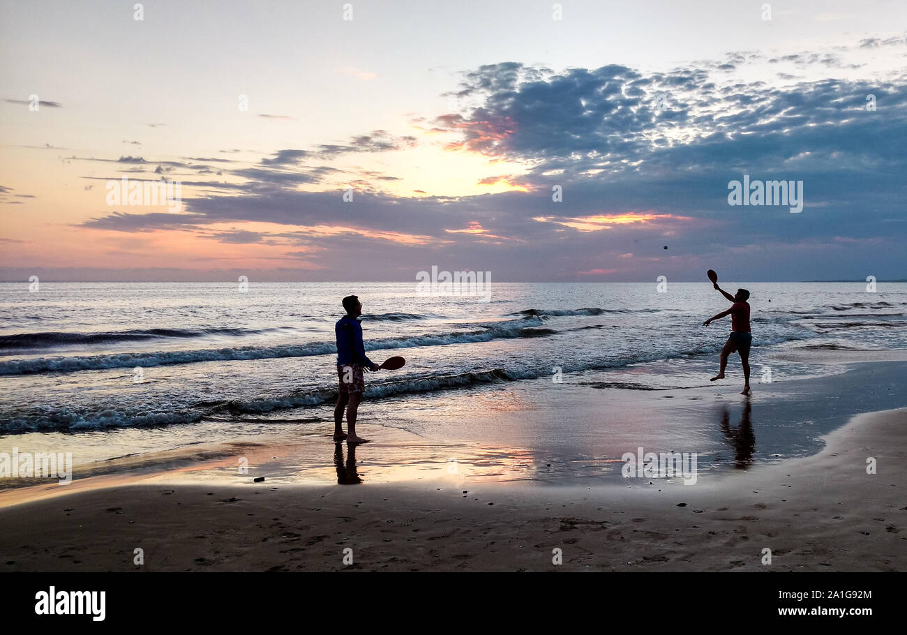 Una coppia omosessuale la riproduzione di pagaia in spiaggia per un bel tramonto Foto Stock