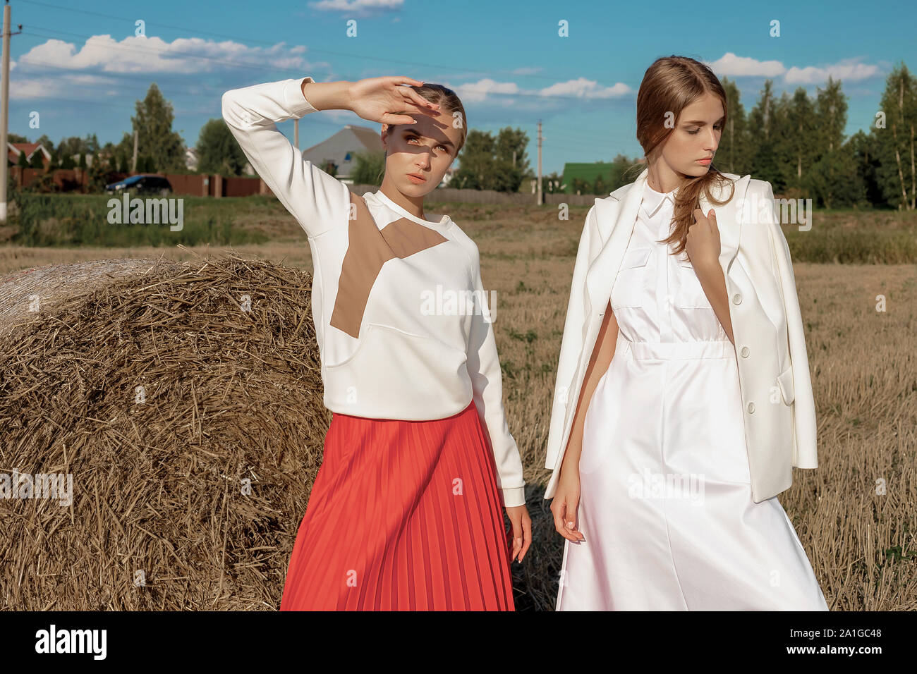 Ritratto di due biondo in ragazze alla moda ed elegante abiti, sullo sfondo di un campo e di una pila di paglia. In una giornata di sole nel mese di agosto Foto Stock