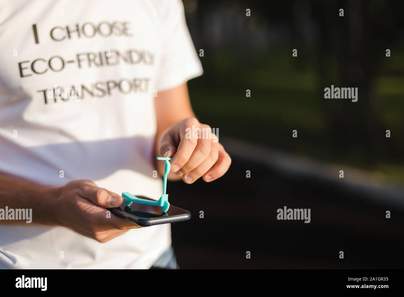 Un uomo tiene nelle sue mani una miniatura del modello di scooter su un display del telefono, eco-friendly Foto Stock