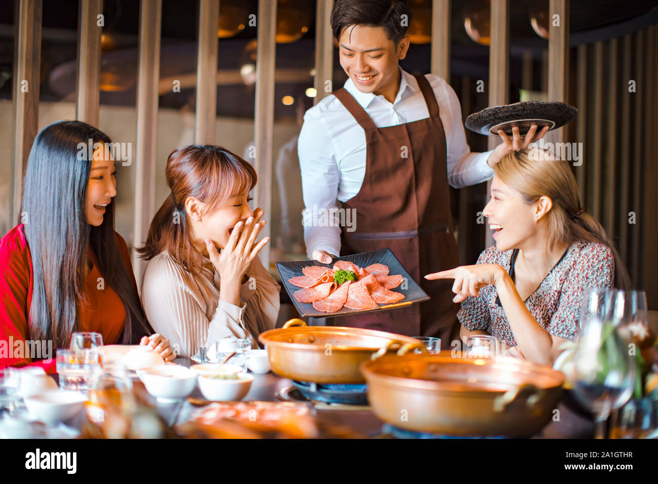 Felice cameriere portare le fette di carne bovina e che serve un gruppo di amici nel ristorante. Foto Stock