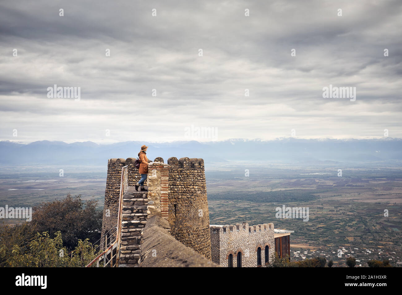 Tourist donna alla fortezza di parete della torre in pietra con vista sulle montagne in Signagi, Georgia Foto Stock