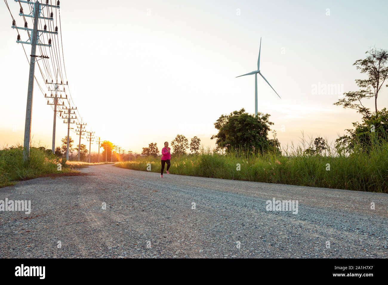 Al tramonto di sera, l'area della turbina eolica genera energia pulita di energia elettrica, una donna è jogging sulla strada. Foto Stock