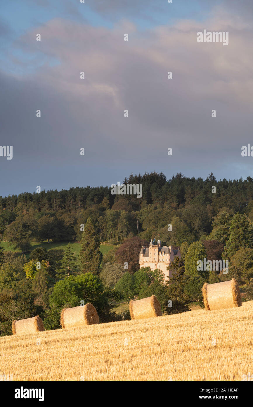Una vista di balle di paglia seduto in un campo di stoppie, con il Castello di Craigievar su un pendio boschivo in background Foto Stock