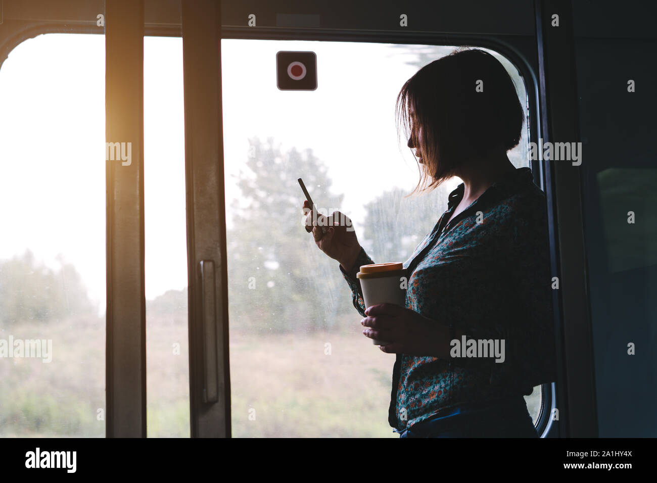 Donna graziosa con un telefono e una tazza di caffè è in piedi in treno Foto Stock