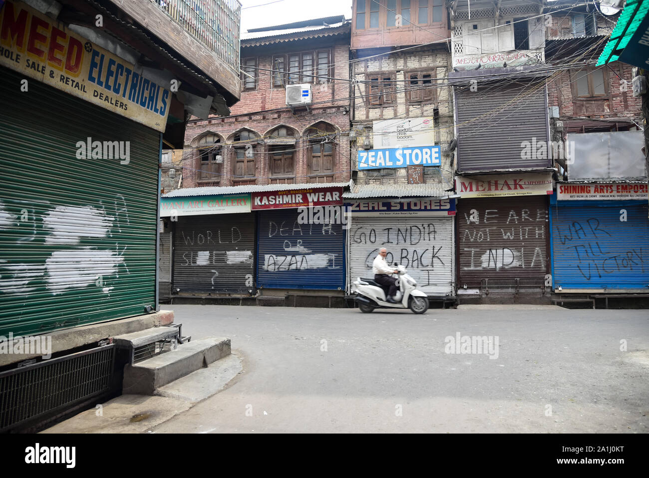 Un motociclista passa di negozi chiusi durante le restrizioni in Srinagar.Dopo la revoca dell'articolo 370 che conferisce lo status speciale di Jammu e Kashmir, le autorità statali hanno imposto restrizioni in Kashmir per prevenire le proteste. Foto Stock