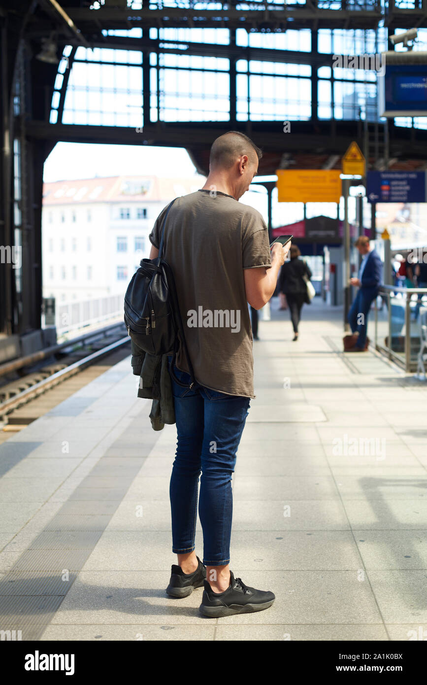 Un giovane uomo caucasico visto da dietro utilizzando uno smartphone in un all'esterno della stazione ferroviaria di Berlino, Germania Foto Stock