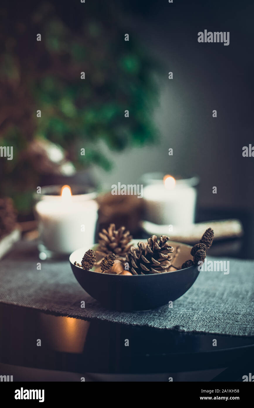 Candele accese e decorazioni naturali di coni, i dadi in vaso nero in tessuto grigio tovagliolo sulla tavola nera. Accogliente atmosfera di casa. Kinfolk Hygge Sl Foto Stock