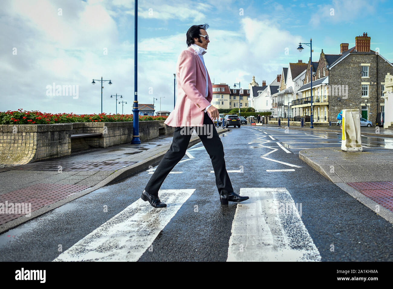 Un Elvis attraversa la strada in direzione di l annuale Porthcawl festival di Elvis in Galles del Sud. La manifestazione richiama migliaia di fan di Elvis alla Welsh cittadina balneare per celebrare il Re del Rock and Roll'. Foto Stock