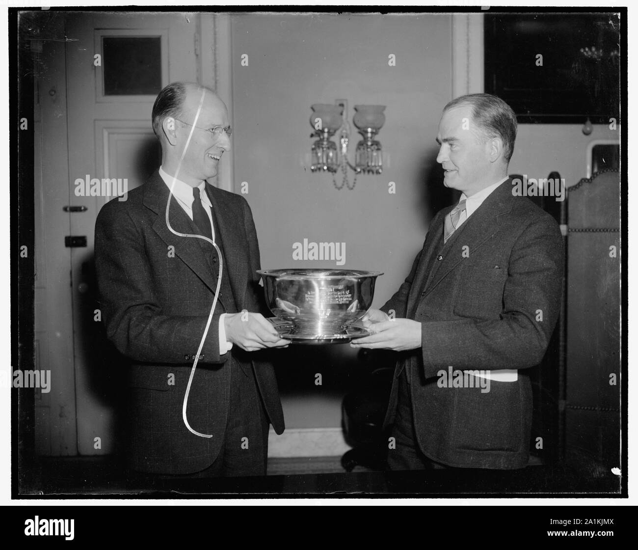 Newsman riceve l'argento punch bowl. Washington D.C., Feb. 25. Come un segno di apprezzamento per il suo aiuto in avente il Congressional premere gallerie rinnovato, il comitato permanente della camera e del Senato di corrispondenti ha presentato oggi un argento Punch Bowl a William K. Hutchinson di International News Service. Nella foto, scattata presso il Campidoglio oggi, Hutchinson è illustrato nella ricezione del vaso da Nathan Robertson (destra) del Re dispone di chi è il presidente del comitato, 25/02/38 Foto Stock
