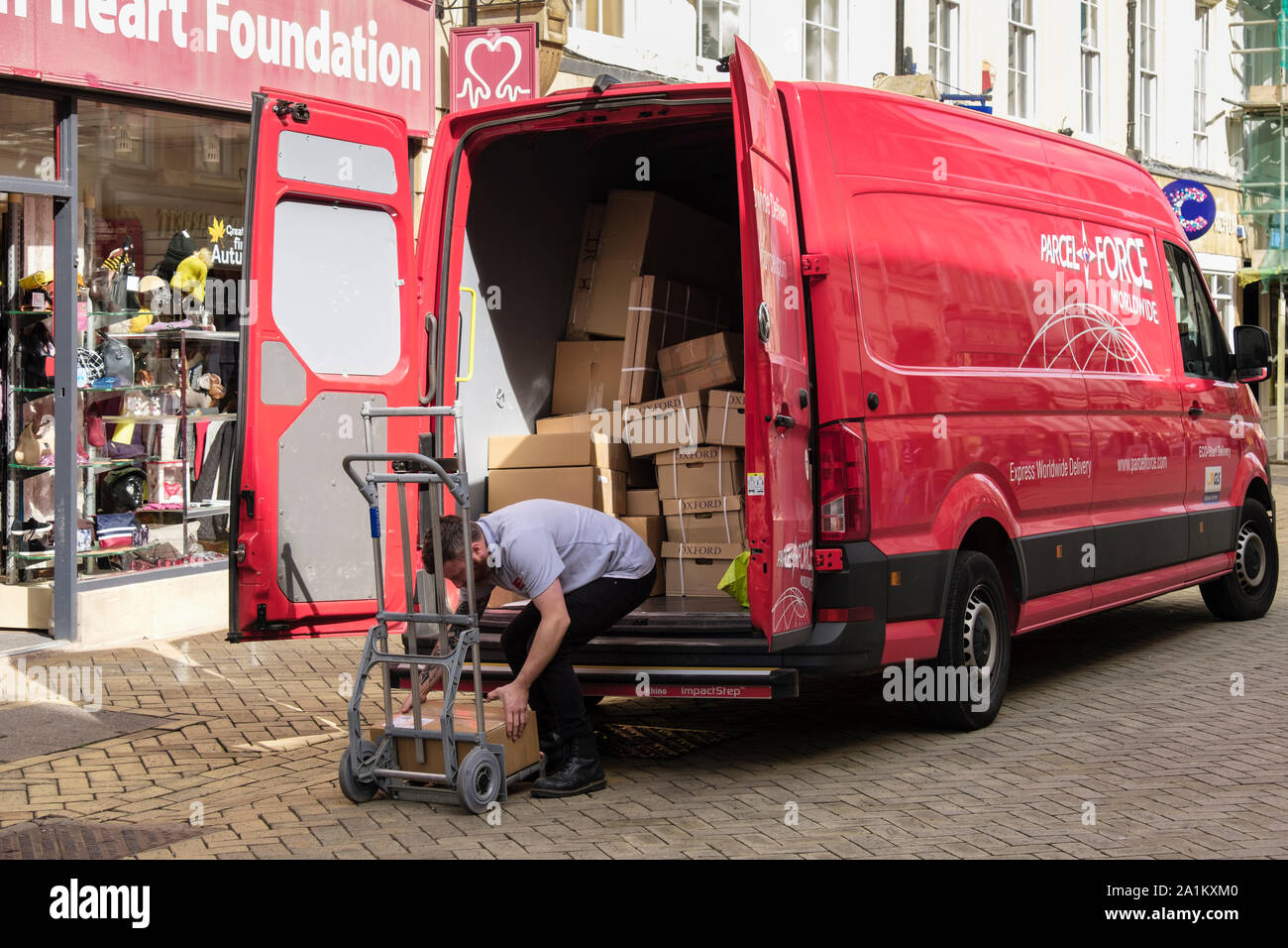 Portalettere facendo una consegna da un pacco vigore furgone pieno di scatole in una strada dello shopping. Stamford, Lincolnshire, Inghilterra, Regno Unito, Gran Bretagna Foto Stock