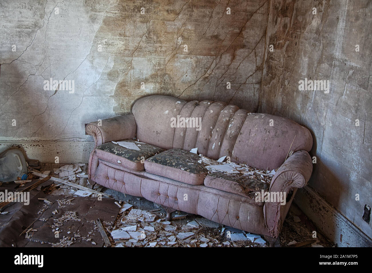 Un vecchio divano Rosa si trova abbandonato tra le macerie di una casa in rovina. Foto Stock
