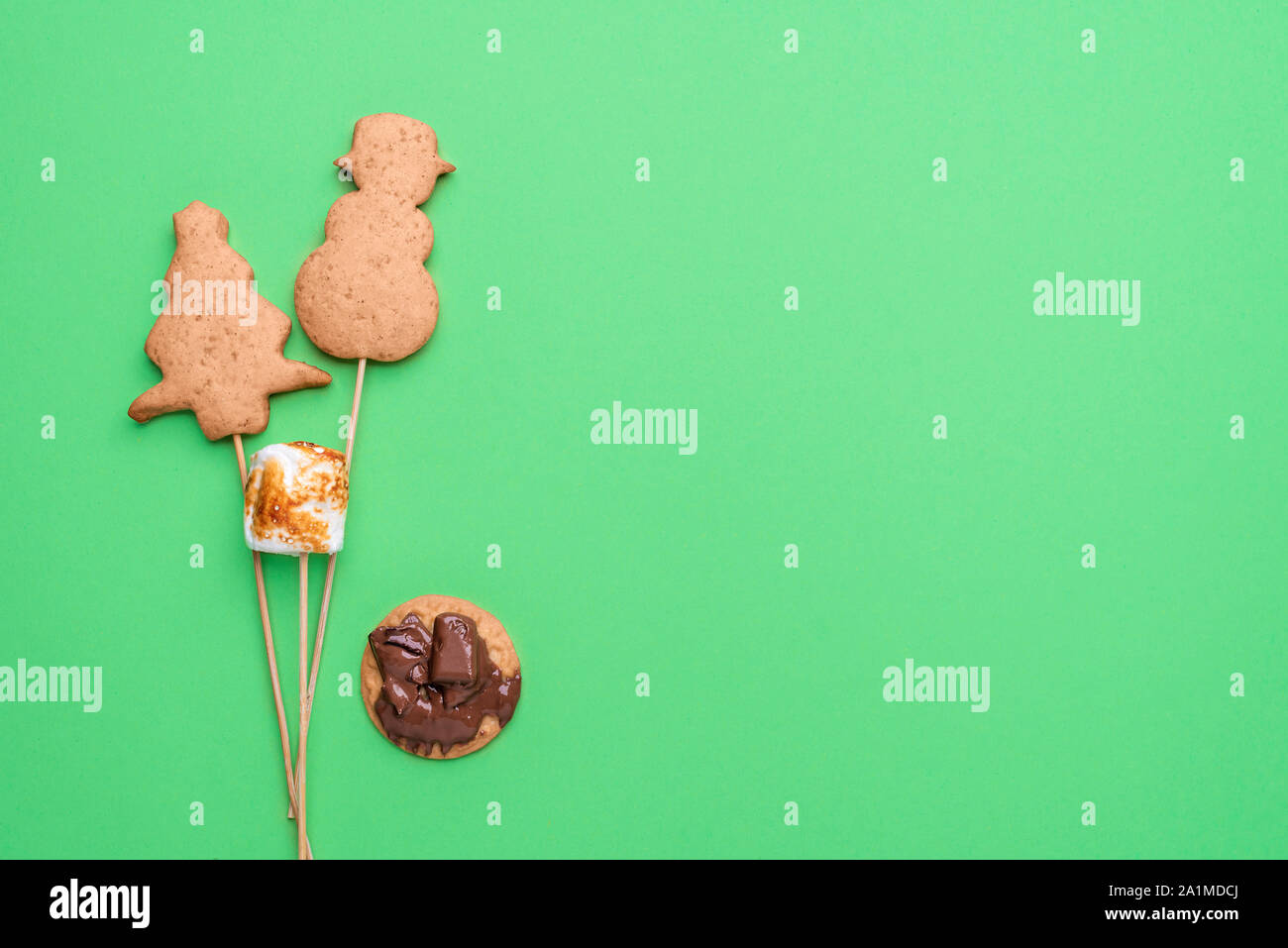 Gingerbread cookie nella struttura ad albero di Natale forma e pupazzo di neve su spiedini con marshmallows e cioccolato fuso su sfondo verde. Biscotti natalizi pop. Foto Stock