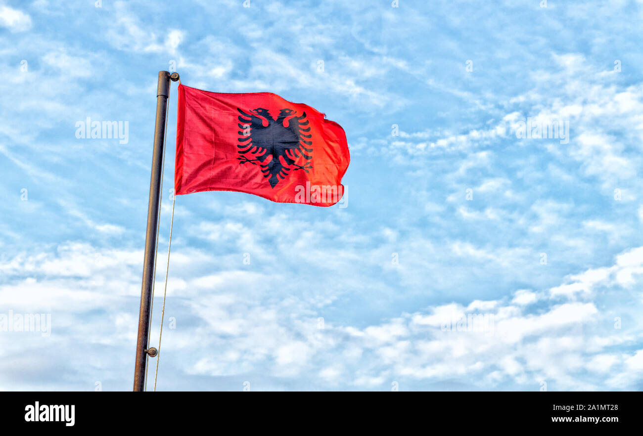 L'Albania bandiera contro il cielo blu con nuvole bianche. La bandiera albanese è una bandiera rossa con un nero stagliano aquila a due teste. L'immagine orizzontale. Foto Stock